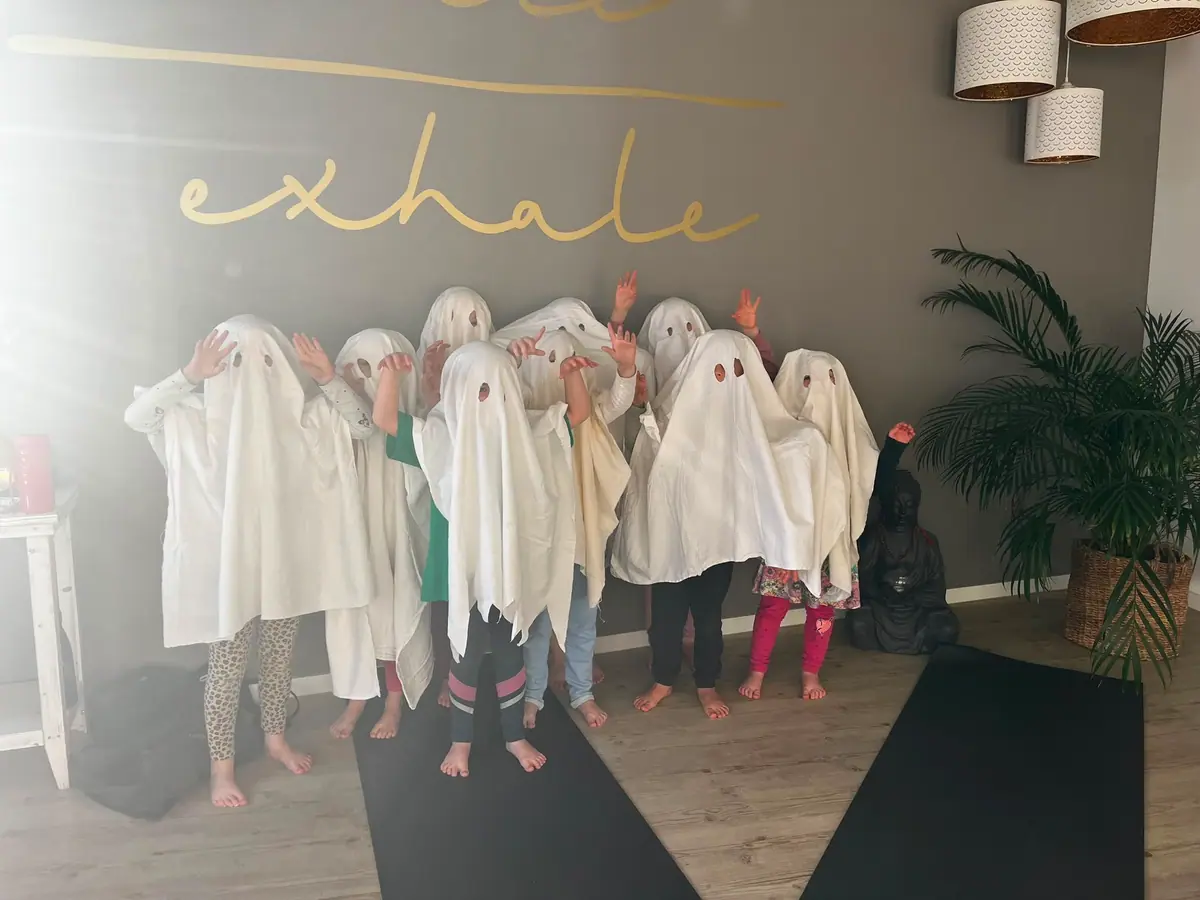 Kinder stehen verkleidet als Gespenster unter weißen Tüchern im Yogastudio