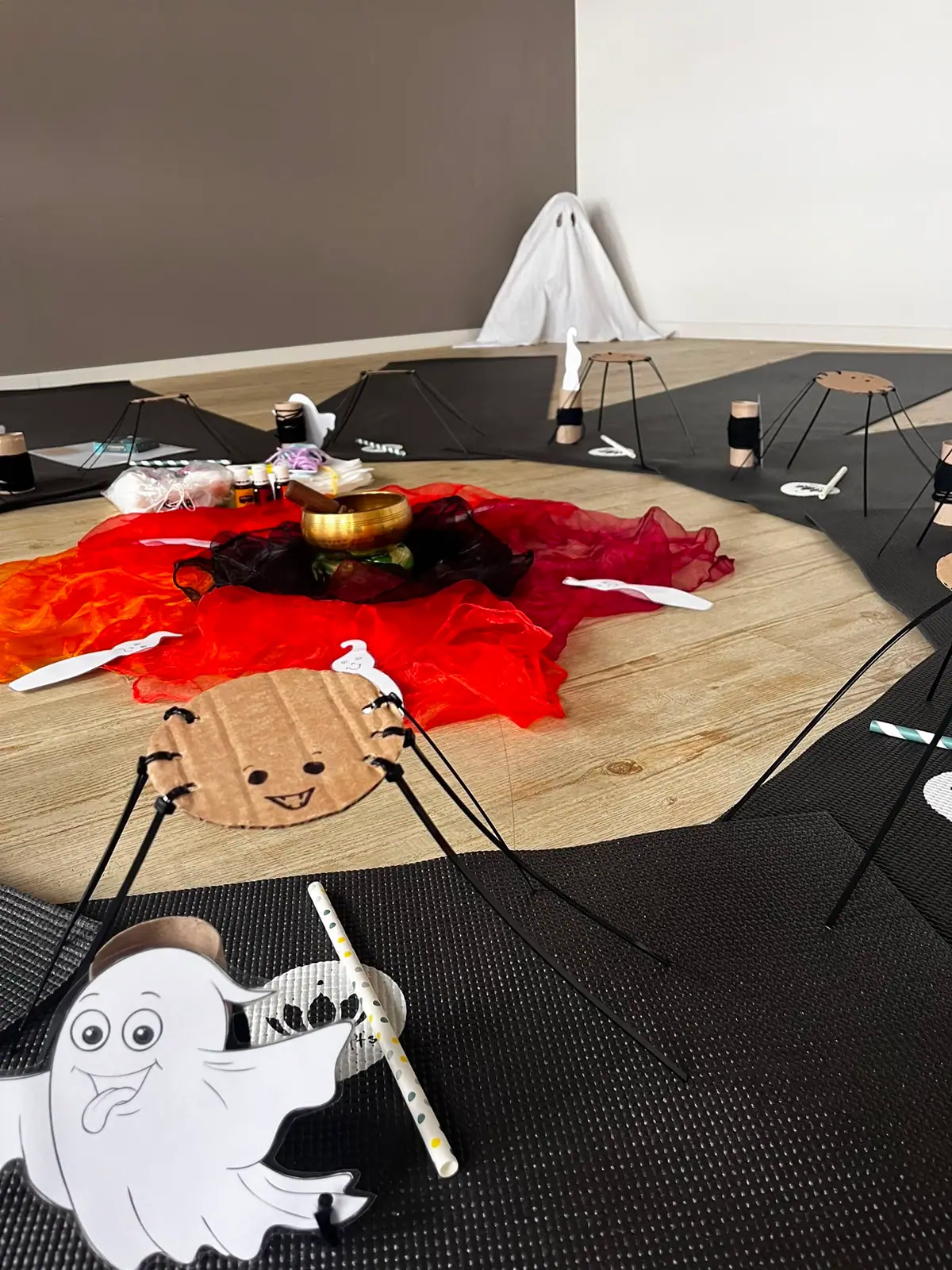 Eine große Spinne aus Pappe liegt auf roten Tüchern im Stundenkreis, davor ein Papp-Gespenst